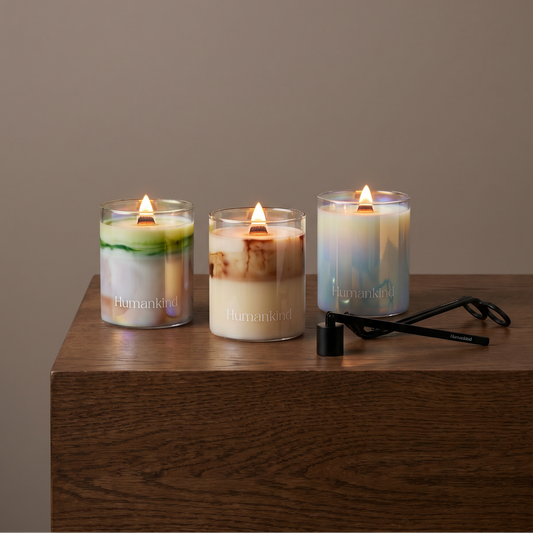 3 candles staged ontop of a wood dresser with a wicker and snuffer in front 